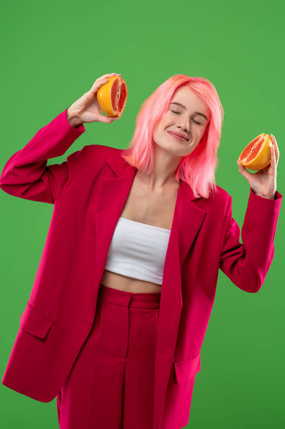 Smiling happy young woman with her eyes closed holding two halves of grapefruit in her hands during the photo shoot - Foto, Imagen