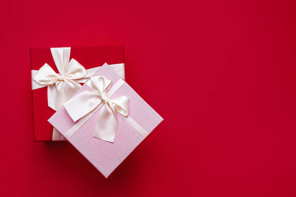 Soft Selective focus on two beautiful gift boxes with satin light ribbon on red background. Pink gift for Christmas, New Year or romantic Valentines Day. Copy space for text. - Fotó, kép