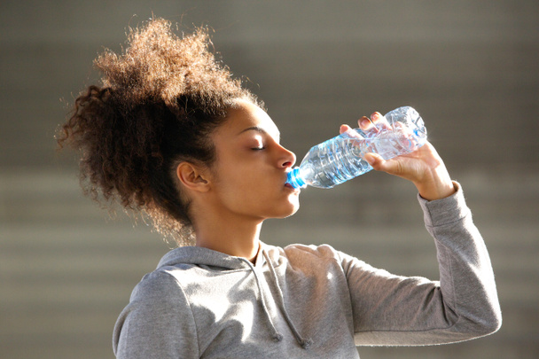 魅力的な若い女性は、ボトルから水を飲む - 写真・画像