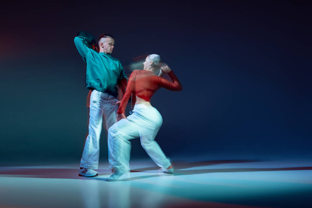 Portrait von jungen Menschen, Mann und Frau tanzen Hip-Hop isoliert vor dunkelblauem Hintergrund mit gemischten Lichtern. Bewegungskonzept, Jugendkultur, aktiver Lebensstil, Action, Streetdance, Hobby, Werbung - Foto, Bild
