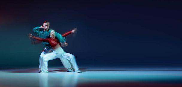 Portrét mladého muže a ženy tančících hip-hopem izolovaných na tmavomodrém pozadí se smíšenými světly. Leták. Koncepce pohybu, kultura mládeže, aktivní životní styl, akce, pouliční tanec, reklama - Fotografie, Obrázek