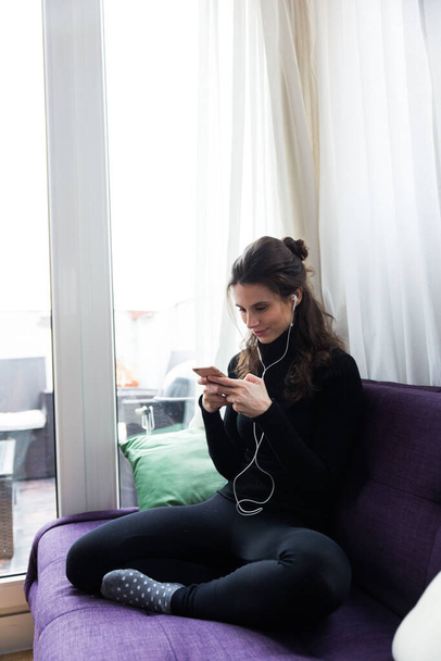 Young adult woman using cellphone indoors while sitting on sofa texting - 写真・画像