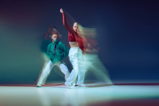 Портрет молодого мужчины и женщины, танцующих на темно-синем фоне со смешанными огнями. Повседневный взгляд. Концепция движения, молодежная культура, активный образ жизни, действия, уличные танцы, реклама - Фото, изображение