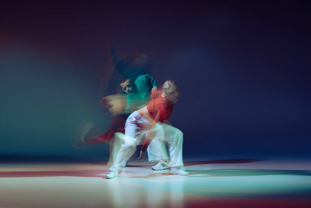 Muotokuva nuoresta miehestä ja naisesta tanssimassa eristettynä tummansinisellä taustalla sekavaloilla. Urheilullinen elämäntapa. Liikkeen käsite, nuorisokulttuuri, aktiivinen elämäntapa, toiminta, katutanssi, mainos - Valokuva, kuva