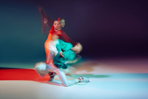 Ritratto di giovane uomo e donna che ballano hip-hop isolato su sfondo viola verde in neon con luci miste. Concetto di movimento, cultura giovanile, stile di vita attivo, azione, street dance, annuncio - Foto, immagini