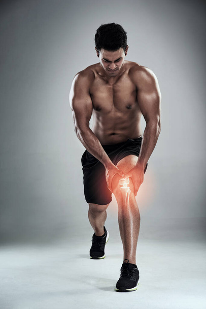 На коліно тисне. Повнометражний знімок спортивного молодого чоловіка, який доглядає поранене коліно на сірому фоні
 - Фото, зображення