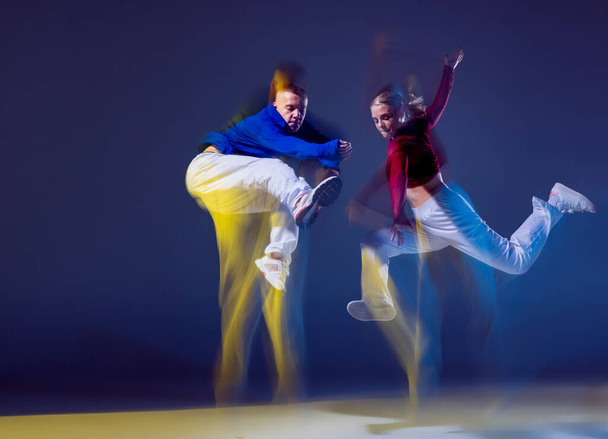 Portrait of young man and woman dancing contemp isolated over dark blue background with mixed lights. Hip-hop culture. Concept of movement, youth culture, active lifestyle, action, street dance, ad - Valokuva, kuva
