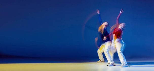 Portrait of young man and woman dancing isolated over dark blue background with mixed lights. Hip-hop. Flyer. Concept of movement, youth culture, active lifestyle, action, street dance, ad - Фото, изображение