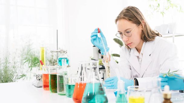 白人女性科学者の研究者は、研究室内の液体の分析のために卒業したシリンダーに物質を滴下するために研究室のドロッパーを使用しています。ドロッパーと卒業したシリンダーで働く科学者. - 写真・画像