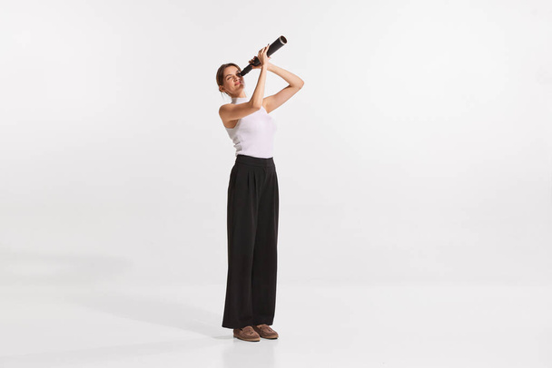 Portrait of young woman looking in telescope isolated over white background. Looking in professional future. Concept of business, IT profession, occupation, economy, personal success, motivation - Photo, image