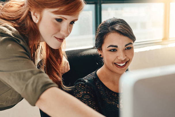 Approche d'une tâche une équipe. deux jeunes femmes d'affaires utilisant un ordinateur ensemble dans un bureau moderne - Photo, image
