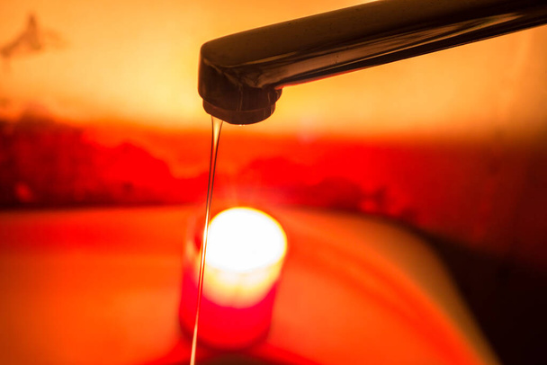 Ohut vesisuihku hanasta palavan kynttilän taustalla. Sähkökatkokset sähkön ja veden Ukrainassa sodan vuoksi - Valokuva, kuva