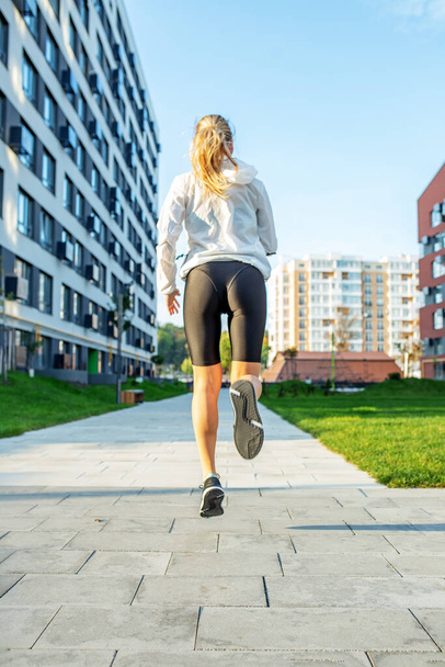 Μια αθλητική νεαρή γυναίκα τρέχει στο πεζοδρόμιο το πρωί. Έννοια του αθλητισμού, υγιεινό τρόπο ζωής και την κατάρτιση. - Φωτογραφία, εικόνα