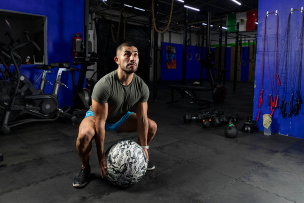 άνδρας σε αθλητικό ντύσιμο γυμνάζεται με μια μπάλα ιατρικής crossfit, σε ένα γυμναστήριο - Φωτογραφία, εικόνα