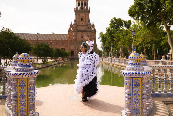 Bailarina flamenca, hermosa adolescente morena vestida con traje típico con volantes y lunares está bailando junto a un canal en una plaza del parque. Concepto flamenco del patrimonio cultural mundial. - Foto, imagen