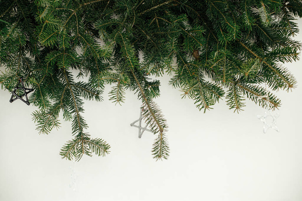 Стильні різдвяні прикраси на ялинових гілках на білому тлі. Сучасні скляні вафлі на гілках ялинки, скандинавське оздоблення в святковій кімнаті, простір для тексту
 - Фото, зображення