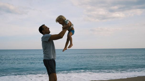Отец бросает своего сына в воздух на пляже замедленной съемки. Высококачественные 4k кадры - Фото, изображение