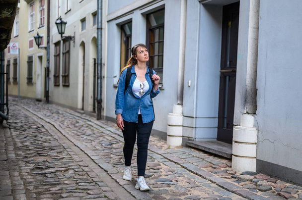 stylish brunette walking along the old street of an ancient european city. - Zdjęcie, obraz