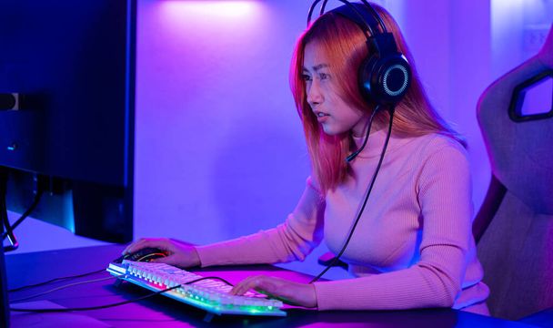 Young woman wearing gaming headphones intend to do playing live stream games online at home, Happy Gamer endeavor plays online video games tournament with computer neon lights - 写真・画像