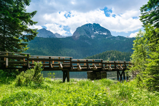 メドピークと氷河ブラック湖を背景にストリーム上の木製の歩道橋。デュルモーター国立公園。湖の近くのウォーキングパスはレクリエーションやハイキングのための人気のある目的地です。モンテネグロ. - 写真・画像