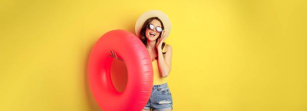 Stylish beach girl with swimming ring, laughing and smiling on summer vacation, sea trip, standing happy against yellow background. - Fotografie, Obrázek