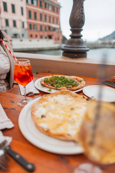 Perhe matkustaa ja istuu kahvilassa pizzan ja cocktailien kanssa Vernazzan vanhassa eurooppalaisessa kaupungissa Italiassa. Pöytä kahdella herkullisella italialaisella pizzalla - Valokuva, kuva
