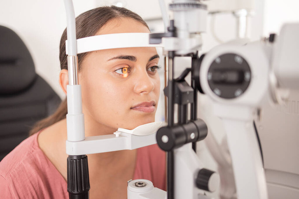Vision, ophthalmology and woman in eye exam with light on iris at eye doctors office. Healthcare, medical insurance and eyes, girl getting healthy visual refraction eye test at ophthalmologist clinic. - Photo, image