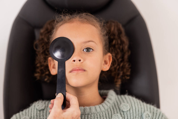 Optométrie, soins oculaires et fille passant un test de vision avec occlusion dans une clinique d'optique médicale. Check-up, optométriste et enfant brésilien faisant un examen de la vue avec un outil optique pour une vision saine - Photo, image