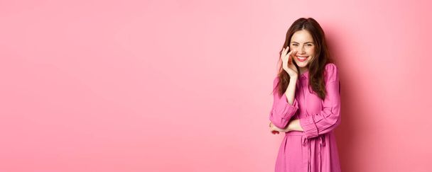 Schönheit und Mode. Attraktive kaukasische Frau kichert und lächelt in die Kamera, posiert in romantischem hellen Kleid an einem schönen Frühlingstag vor rosa Hintergrund. - Foto, Bild