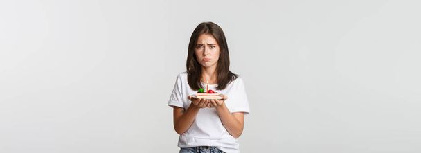 Miserable birthday girl looking sad, holding b-day cake with candle. - Photo, Image
