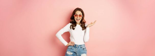 Coquettish and stylish brunette girl, laughing and smiling, wearing sunglasses, wearing white blouse and jeans, pink background. Copy space - Foto, afbeelding