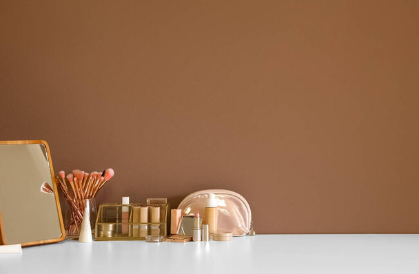 Різні косметичні засоби та пензлі для макіяжу на столі біля кольорової стіни
 - Фото, зображення