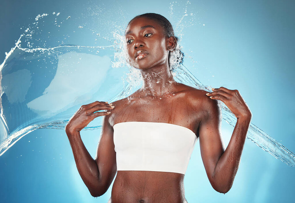 Splash, skincare and black woman with water for wellness, beauty and dermatology against blue studio background. Spa, thinking and African girl model with idea for fresh, natural and body hydration. - Fotoğraf, Görsel