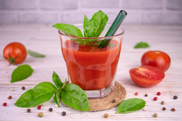 Tomatensap met specerijen in een glas op een witte houten achtergrond. - Foto, afbeelding