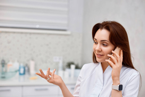 happy female beautician speaking on a smartphone in beauty salon. - Fotografie, Obrázek