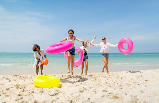 Amplio grupo de chicas adolescentes llevar anillo de natación y correr desde el mar de vuelta a la playa durante las vacaciones o tiempo de relajación de vacaciones. - Foto, imagen