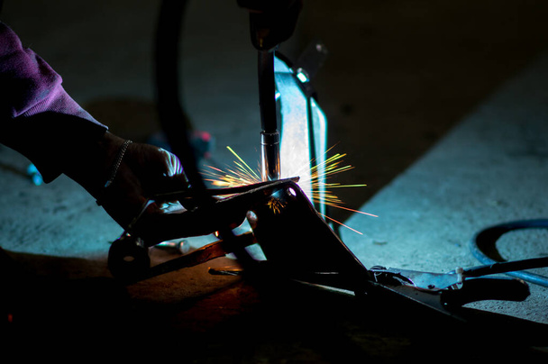 συγκολλητής στο σκοτάδι εκτελεί εργασίες συγκόλλησης στο μέταλλο με μηχανή συγκόλλησης - Φωτογραφία, εικόνα