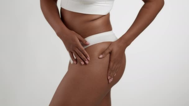 Huidproblemen. close-up shot van onherkenbare zwarte vrouw in ondergoed tonen cellulitis op haar heupen, poseren over witte studio achtergrond, slow motion - Video
