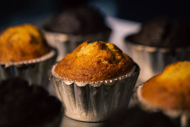 Muffins fraîchement cuits dans des moules métalliques en gros plan dans une boulangerie sur un fond sombre et flou. - Photo, image