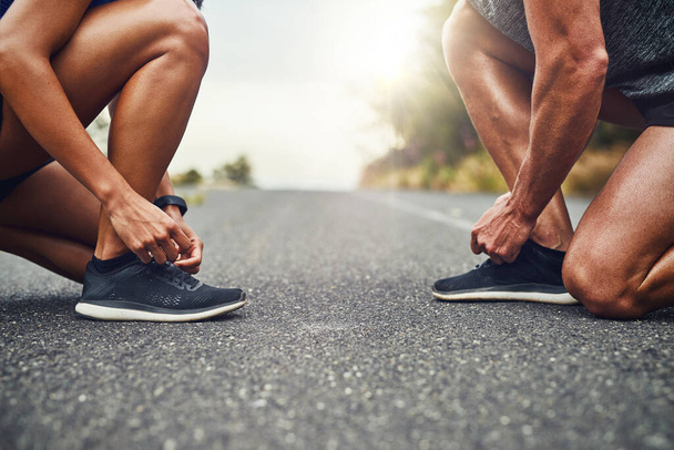 Asegurar nuestros zapatos antes de correr. una pareja irreconocible entrenando para un maratón al aire libre - Foto, imagen