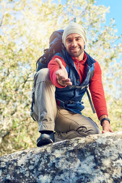 Need a hand. Portrait of a happy hiker extending his hand while sitting on top of a rock on the trail - Foto, imagen