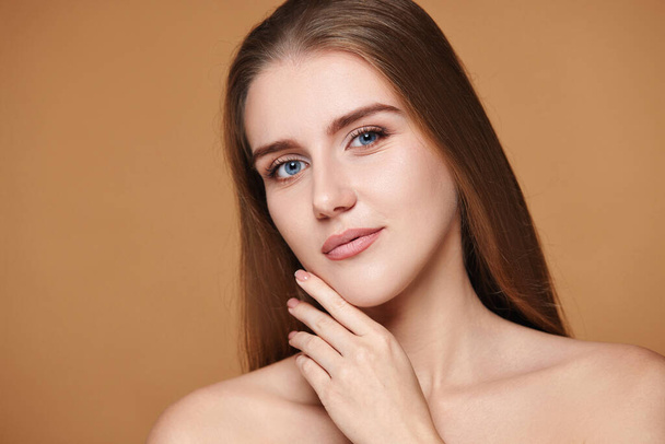 young brunette woman touching cheeks and enjoy perfect skin on beige background - Zdjęcie, obraz