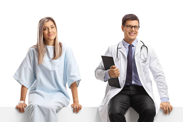 Male doctor and a female patient sitting on a blank panel isolated on white background - Fotó, kép