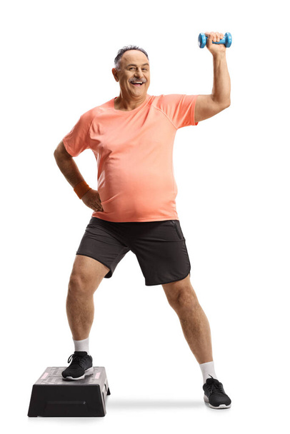 Full length portrait of a mature man exercising step aerobic with a small weight isolated on white background - Фото, изображение