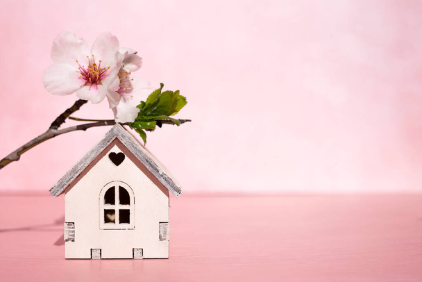 Petite maison en bois et branche de sakura sur fond rose. Vue latérale, espace pour le texte. - Photo, image