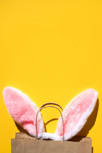 Rabbit ears stick out of a paper bag on a yellow background. Flat lay, vertical image. - Foto, imagen