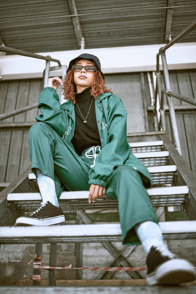 Woman, street fashion and model in city for trendy gen z portrait. Freedom, urban lifestyle and young black girl with stylish hip hop clothes, sunglasses and hat on building stairs in urban town. - 写真・画像