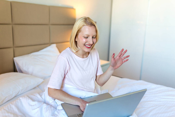 Attraktive Frau im weißen Hemd mit Laptop und lächelnd am Morgen. Video-Chat und freiberufliche Arbeit von zu Hause aus Konzept der schönen jungen Frau mit Laptop im Bett - Foto, Bild