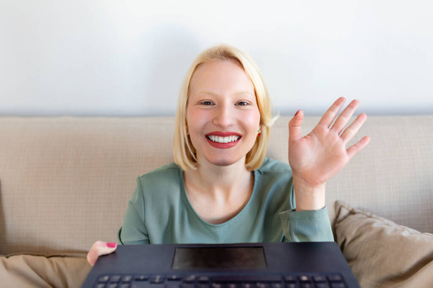 Young woman waving at laptop and talking to her friends via video call, girl student talking by video conference call, female teacher trainer tutoring by webcam, online training, e-coaching concept - Foto, Bild