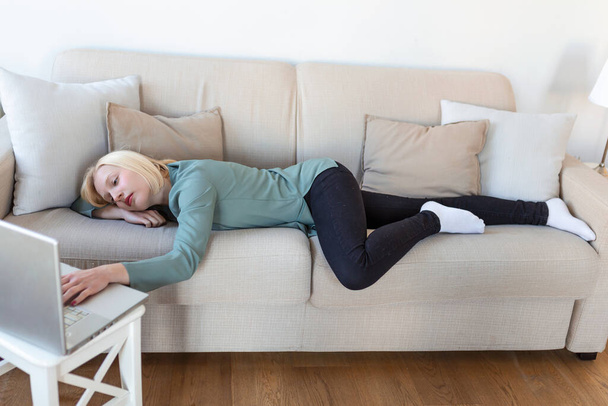 Erschöpfte junge Frau auf Sofa liegend, Laptop benutzend, zu müde oder gelangweilt von der Online-Arbeit zu Hause, freier Raum. Workaholismus, chronische Müdigkeit, Überarbeitung des Fernarbeitskonzepts - Foto, Bild